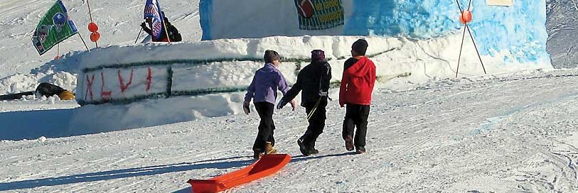 Kids dragging a sled up a hill next to a massive snow fort
