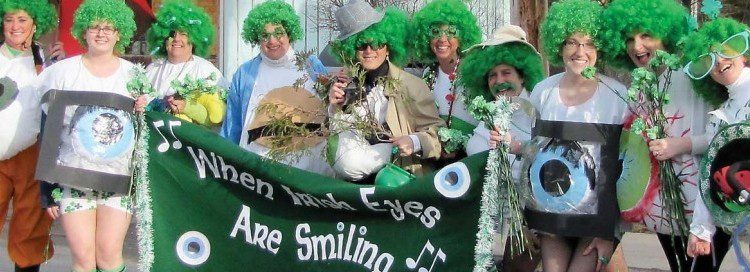 People in a line smiling with green wigs and st Patricks day items holding a green banner that say when Irish eyes are smiling