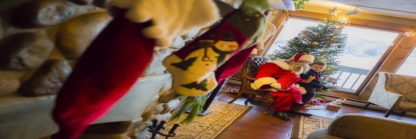 A picture of kids on Santas lap with a fireplace with stockings and a tree with Christmas decorations