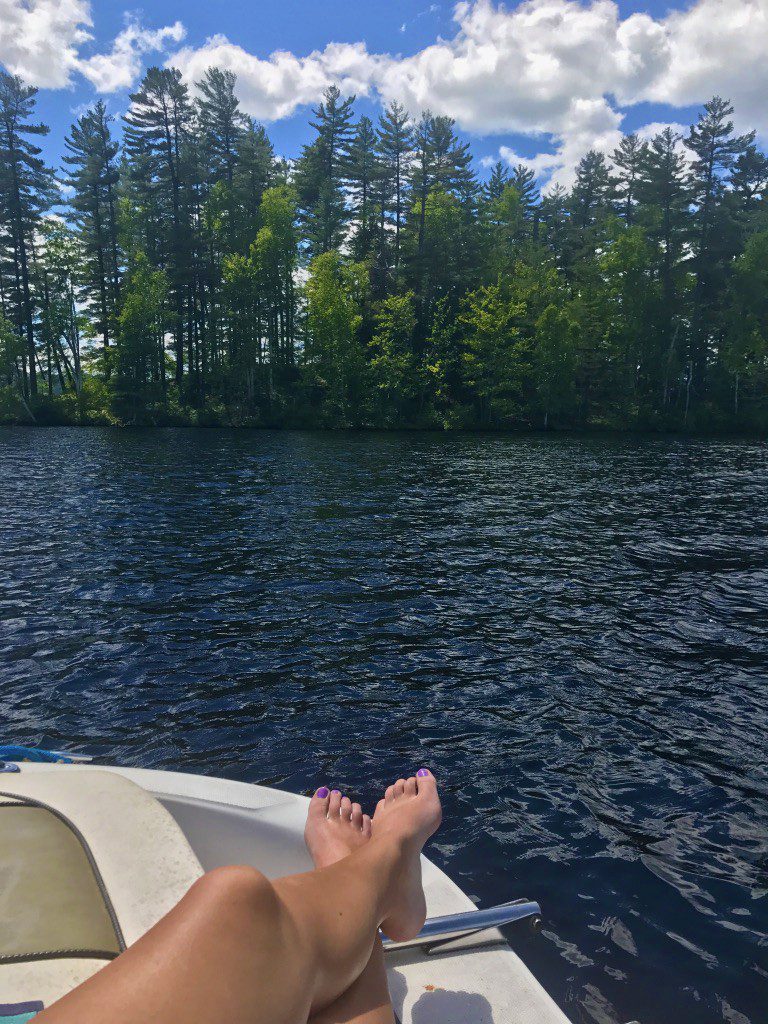 someones feet resting on the boat with the lake and trees beyond