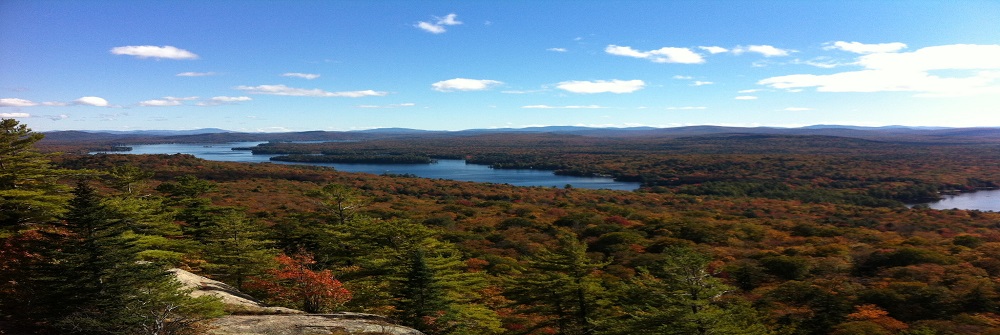 A view from the top of a mountain of fall foliage and calm clear lakes