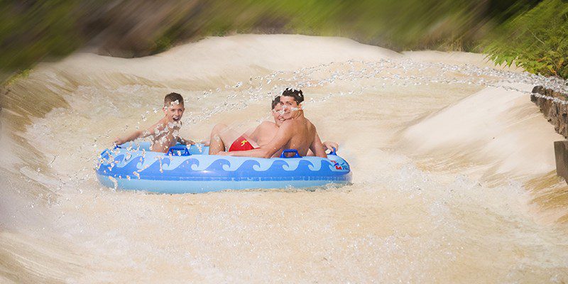 Kids smiling on a tube on their way down a waterslide with water spraying over them